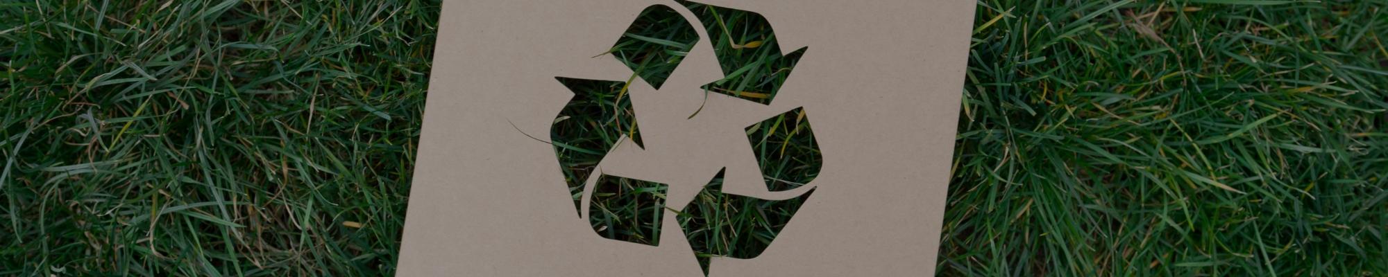 Recycling symbol cut out of cardboard on grass.
