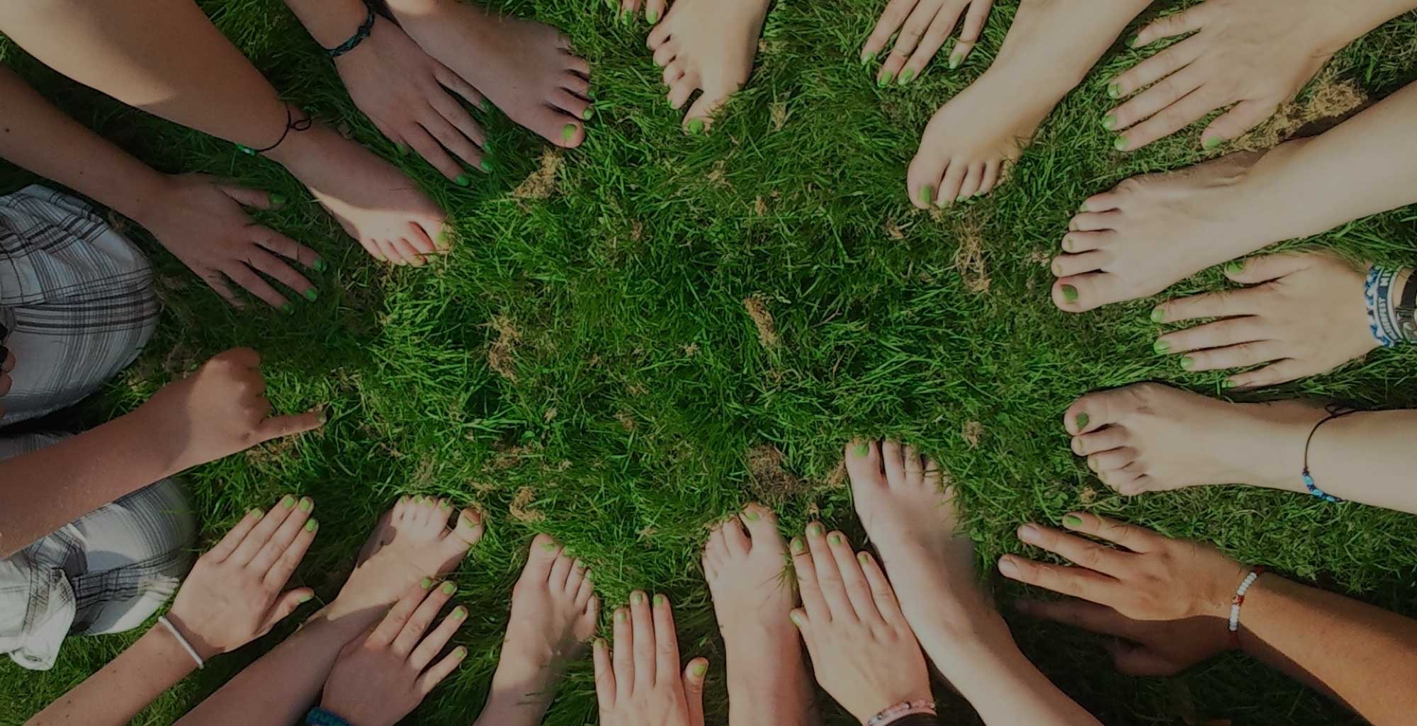 Image of people's hands and feet in the grass.