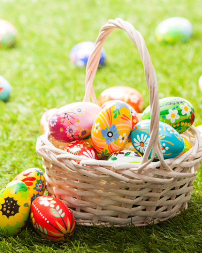 Image of easter basket filled with easter eggs on the grass with several easter eggs scattered throughout the grass.
