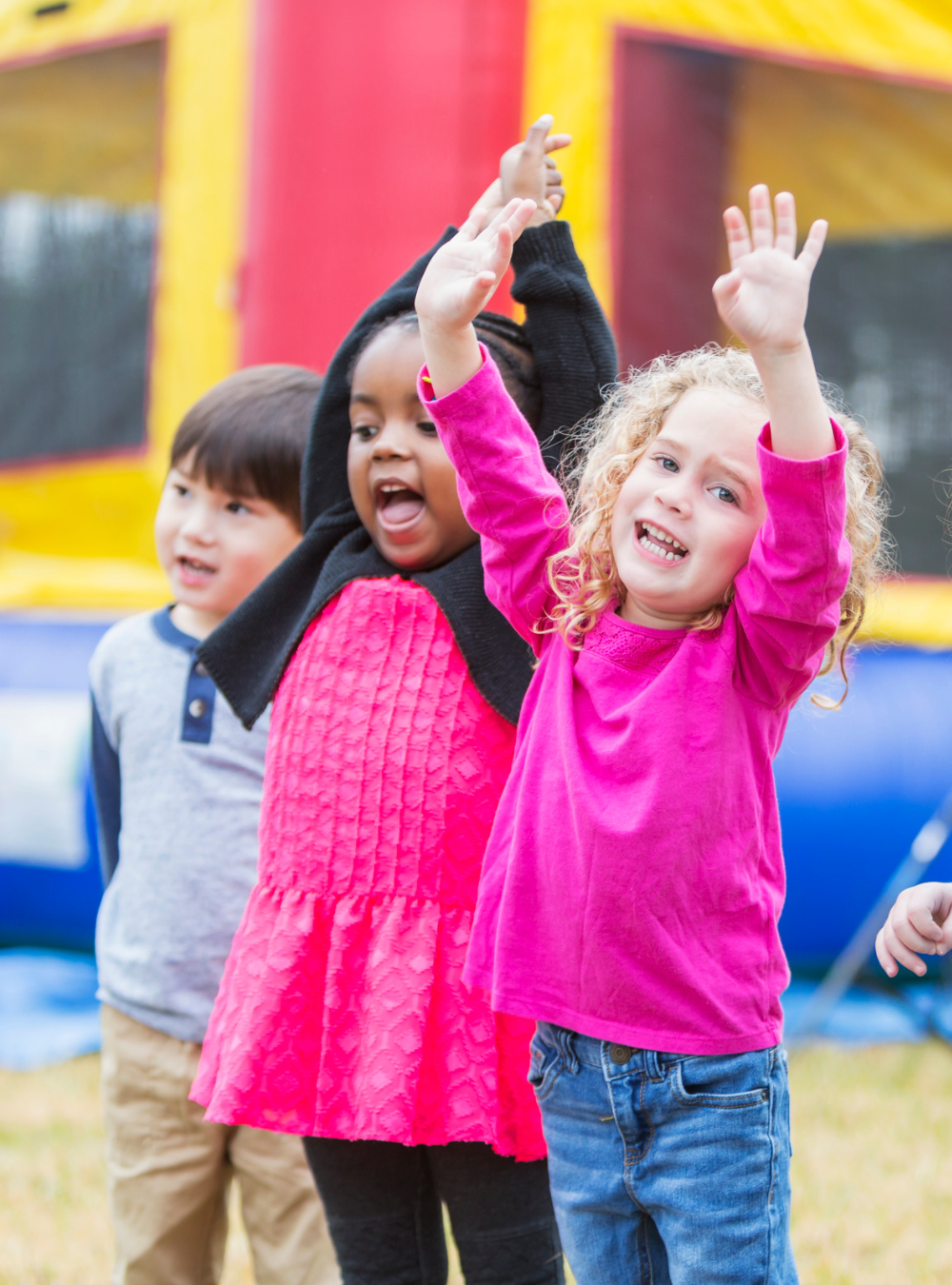 Three children standing in front of a bounce house having fun.