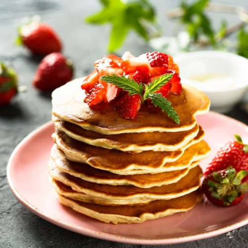 Image of a stack of pancakes with fruit on it and images being poured over.