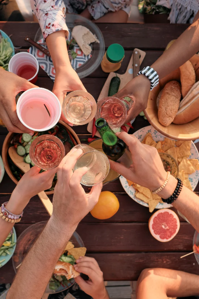 Overhead image of people sitting around a picnic table with lots of food clinking glasses