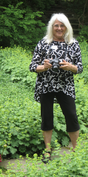 Image of Ann in the garden holding a camera.