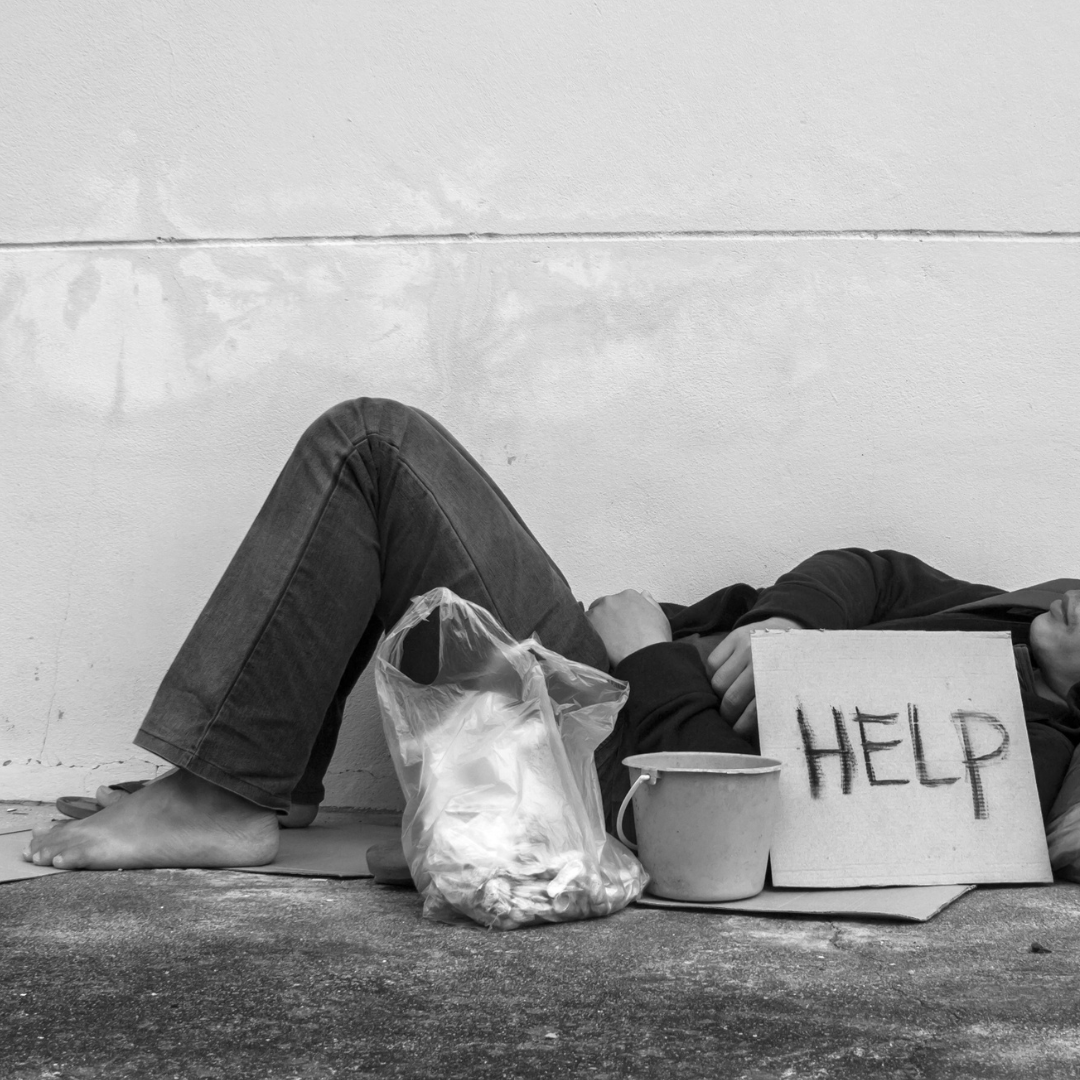 Image of a person sleeping on the street with a sign that says "help"