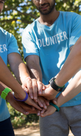 Image of people wearing volunteer shirts in a circle with their hands together.