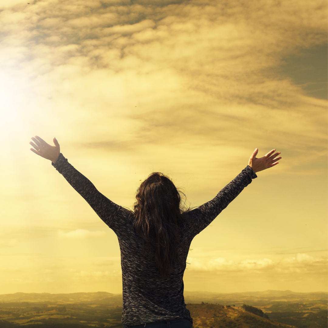 Image of a woman facing the sun with her arms reaching to the sky