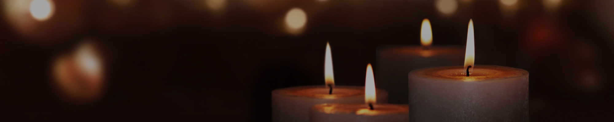 image of four lit candles in the forefront and several blurred lit candles in the background